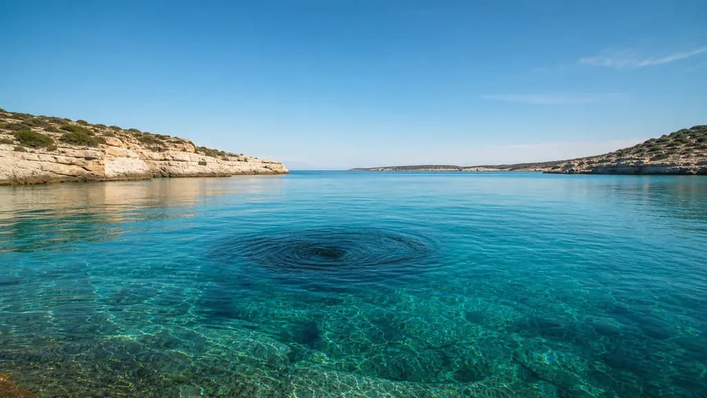 A calm turquoise bay under blue sky with a subtle dark whirlpool turning near its center.