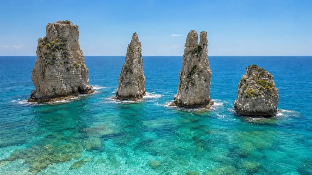 Four differently shaped sea stacks rising together from bright turquoise water under a clear sky.