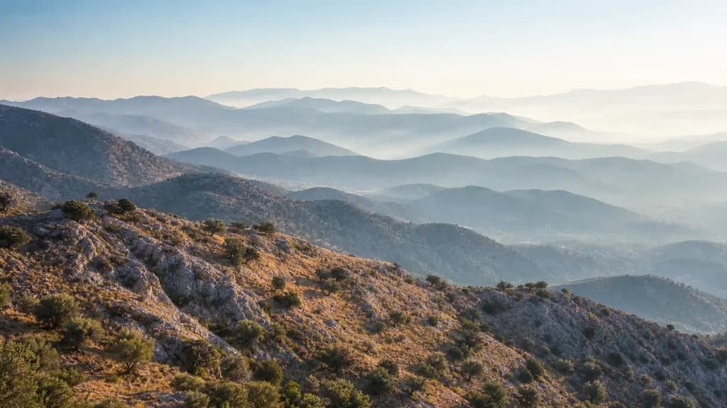 Layered mountain ridges fading from a sharp sunlit foreground into pale haze in the distance.